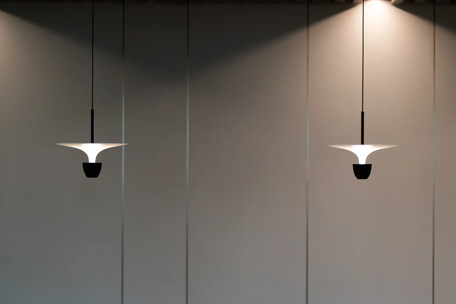 Two pendant lights with sculptural white shades against a grey wall